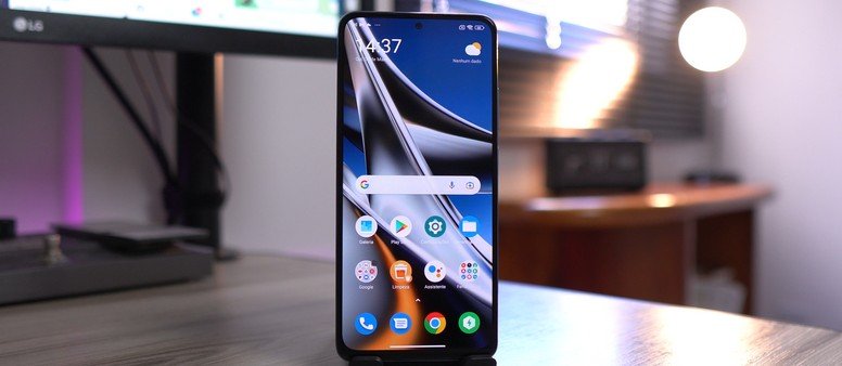 Smartphone em uma mesa de trabalho com a tela inicial exibindo o Novo Poco Launcher e seus ícones de aplicativos.