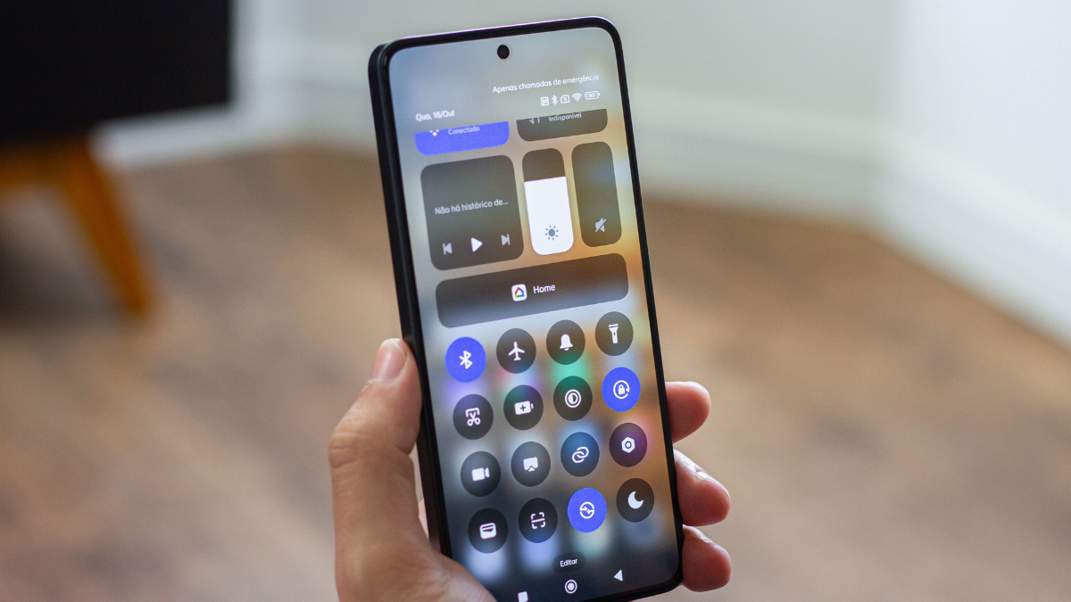Uma mão segura um smartphone Xiaomi que exibe a interface de usuário do Android 16 na central de controle, mostrando os atalhos para conectividade e controle de casa inteligente.