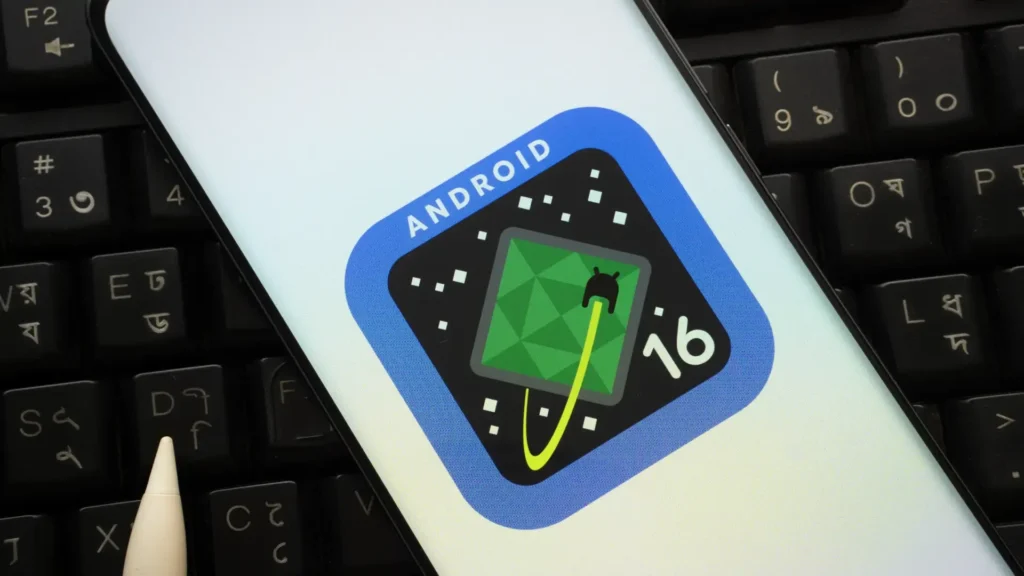 Um smartphone exibe o logotipo do Android 16. O logotipo é um quadrado azul arredondado com um quadrado preto dentro. Dentro do quadrado preto, há um padrão geométrico verde claro que se assemelha a um terreno montanhoso visto de cima. Um cabo amarelo e verde neon está conectado ao "Android" estilizado dentro do quadrado preto. O número "16" branco está posicionado no canto inferior direito do quadrado preto. O smartphone está parcialmente sobreposto a um teclado preto com letras brancas e caracteres adicionais em outra cor (possivelmente bengali). Uma caneta stylus branca também está visível no canto inferior esquerdo.