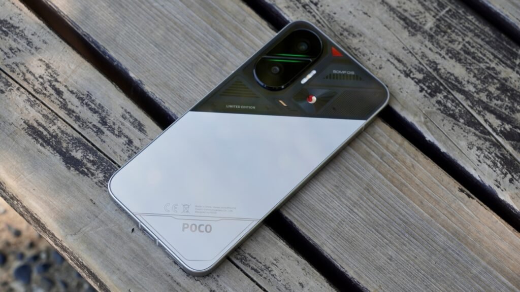 Um smartphone POCO F7 prateado sobre uma superfície escura e texturizada. A câmera traseira dupla e o logo da POCO são visíveis.